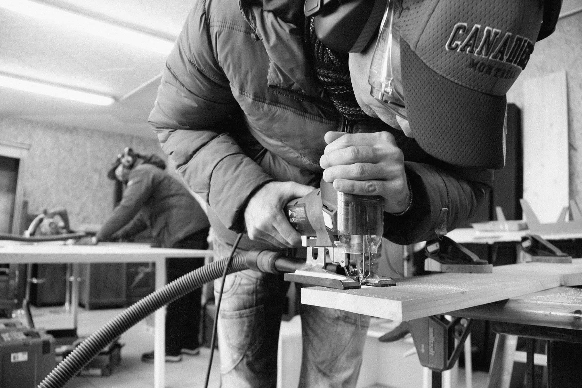 Photo en noir et blanc d'un apprenti sciant une planche