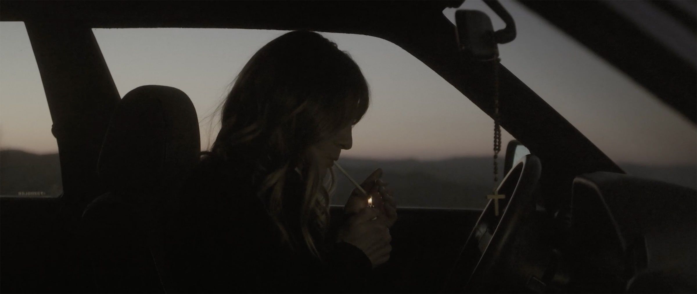 capture d'un plan de film, une femme allume une cigarette au volant d'une voiture