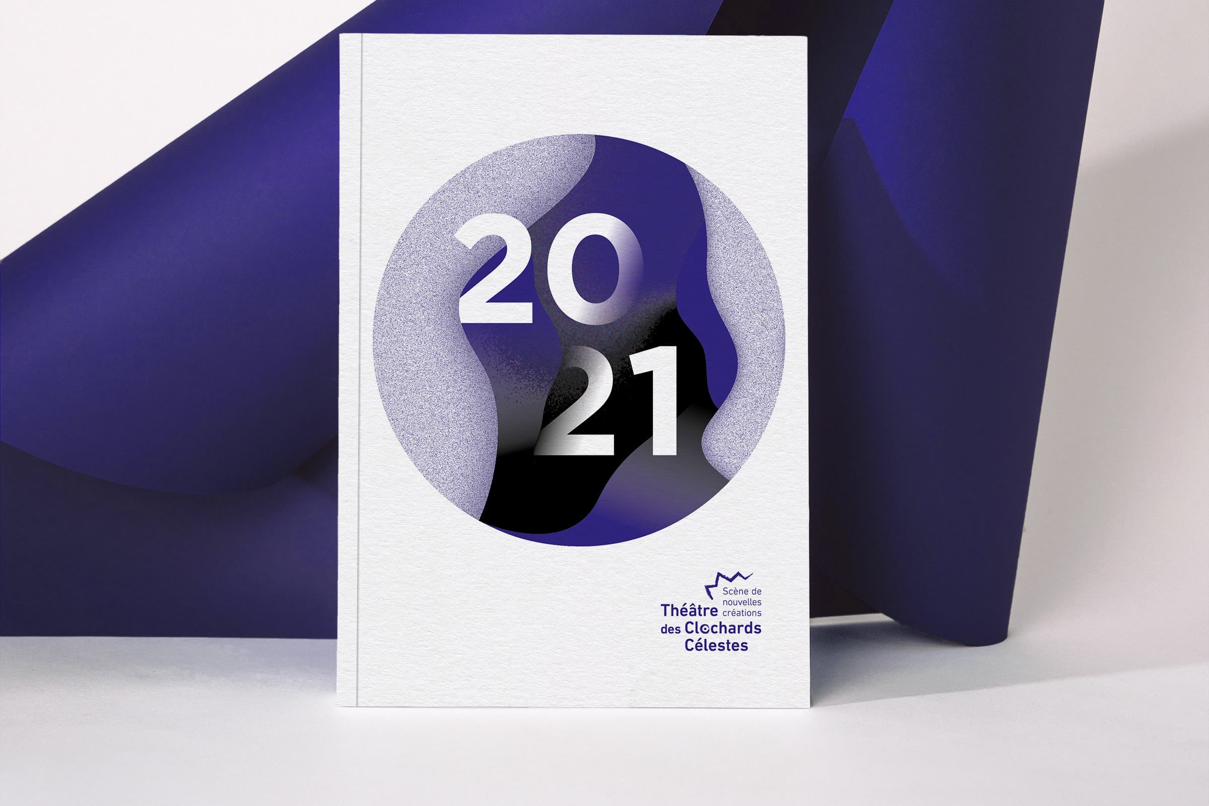 Programme de la saisons 2021 posée debout devant un papier bleu roulé